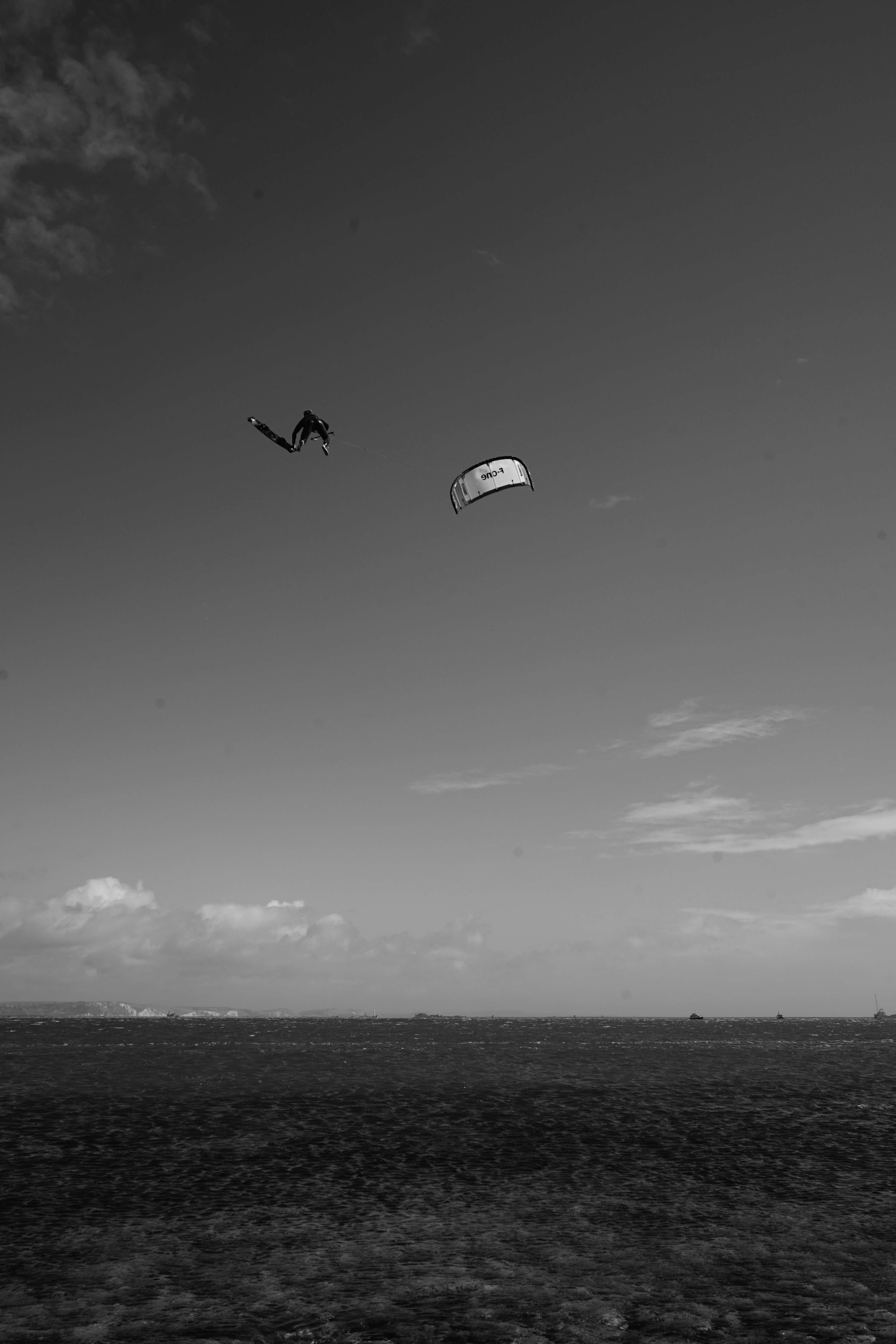 A kiteboarder fully airborne over the sea at Chesil Beach, kite overhead, mid grab.